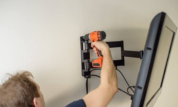 A person using a cordless drill to fix a full-motion TV mount into a wall.