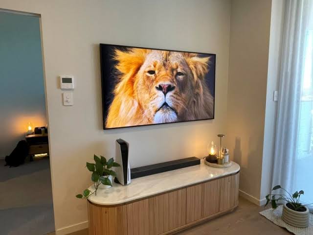 A framed-style TV on a wall above a timber console with a soundbar.
