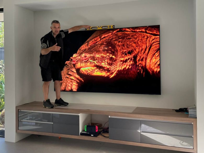 A very large TV mounted above a floating console, checked with a spirit level.